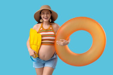 Mavi arka planda yüzüklü, şişme yüzüklü hamile bir kadın. Seyahat kavramı