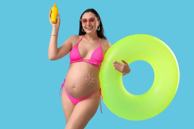 Güneş kremi ve mavi arka planda şişirilebilir yüzüğü olan hamile bir kadın. Seyahat kavramı