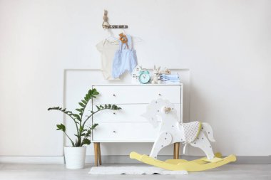 Şık çocuk odasının içinde sallanan at, elbise ve bebek kıyafetleri ışık duvarında asılı.