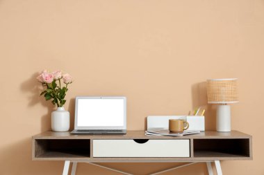 Modern dizüstü bilgisayarı ve bej duvarın yanında güzel çiçekleri olan şık bir çalışma alanı
