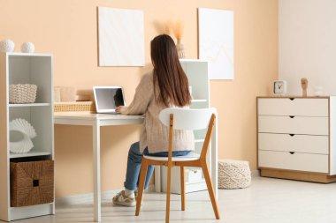 Modern dizüstü bilgisayarı ve ev ofisinde güzel çiçekleri olan şık bir çalışma alanında çalışan genç bir kadın.