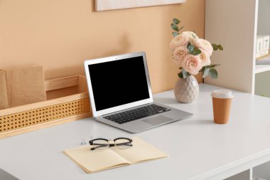 Modern dizüstü bilgisayarlı şık çalışma alanı, ev ofisinde bir fincan kahve ve güzel çiçekler, yakın plan.