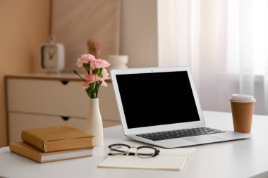 Modern dizüstü bilgisayarı, bir fincan kahvesi ve güzel çiçekleri olan şık bir çalışma alanı.