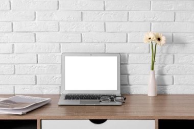 Modern dizüstü bilgisayarı ve beyaz tuğla duvarın yanında güzel çiçekleri olan şık çalışma alanı