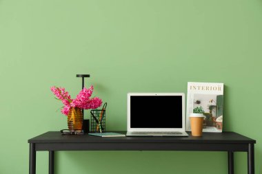 Modern dizüstü bilgisayarı ve yeşil duvarın yanında güzel çiçekleri olan şık çalışma alanı