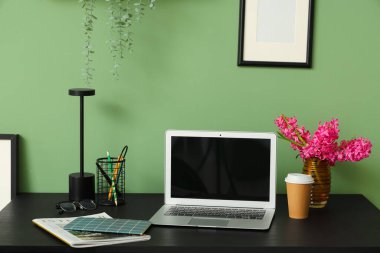 Modern dizüstü bilgisayarı ve yeşil duvarın yanında güzel çiçekleri olan şık çalışma alanı
