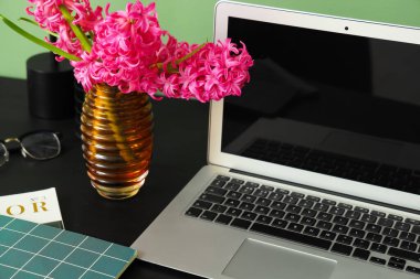 Modern dizüstü bilgisayarı ve yeşil duvarın yanında güzel çiçekleri olan şık bir çalışma alanı.