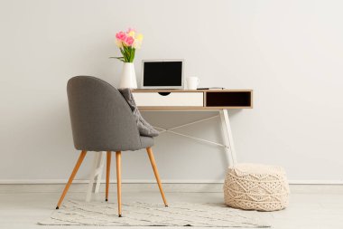 Modern dizüstü bilgisayarı ve beyaz duvarın yanında güzel çiçekleri olan şık çalışma alanı