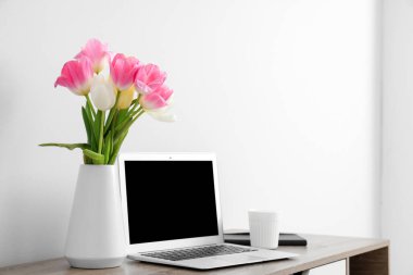 Modern dizüstü bilgisayarı ve beyaz duvarın yanında güzel çiçekleri olan şık çalışma alanı
