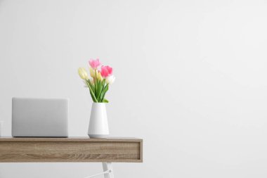 Modern dizüstü bilgisayarı ve beyaz duvarın yanında güzel çiçekleri olan şık çalışma alanı