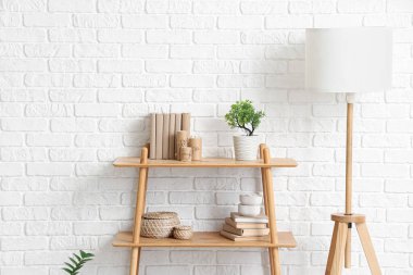 Salonda beyaz tuğla duvarın yanında raf ve lamba var.