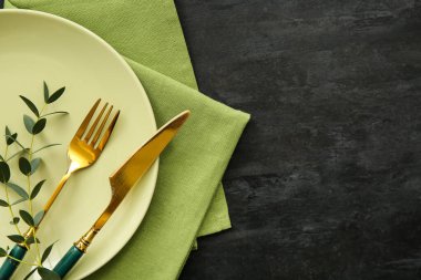 Siyah grunge arka planında çatal bıçak, peçete ve okaliptüs tabağı.