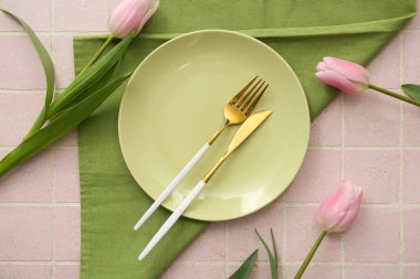 Çatal bıçak takımı, peçete ve pembe fayanslı laleler.