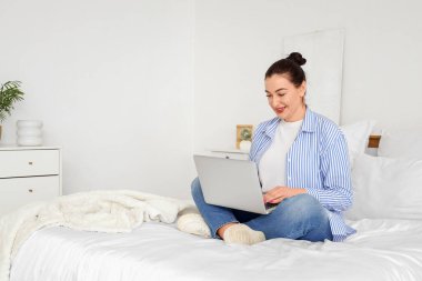 Yatak odasında dizüstü bilgisayar kullanan güzel kadın.
