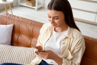 Evdeki koltukta cep telefonu kullanan güzel genç bir kadın.