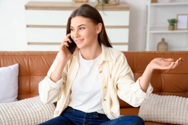 Evdeki kanepede cep telefonuyla konuşan güzel genç bir kadın.