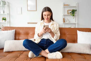 Evdeki koltukta cep telefonu kullanan güzel genç bir kadın.