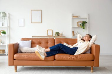 Evdeki kahverengi kanepede uzanmış güzel genç bir kadın.