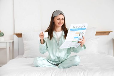 Elinde kahve fincanıyla yatak odasında gazete okuyan güzel genç bir kadın.