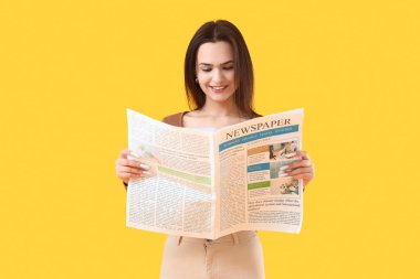 Burnu delinmiş, sarı arka planda gazete okuyan genç bir kadın.