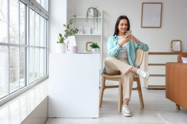 Burnunda piercing olan genç bir kadın evde cep telefonu kullanıyor.