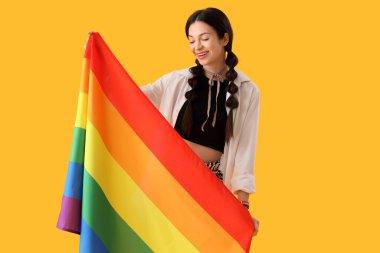 Sarı arka planda gökkuşağı bayrağı olan güzel genç bir kadın. LGBT kavramı