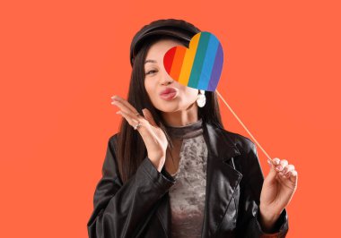 Gökkuşağı kalpli güzel bir kadın turuncu arka planda öpüşüyor. LGBT kavramı