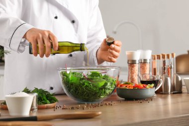 Erkek aşçı mutfaktaki masada sebze salatasına zeytinyağı döküyor.