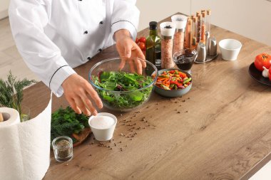 Mutfaktaki masada tuzlu sebze salatası hazırlayan erkek aşçı, yakın plan.