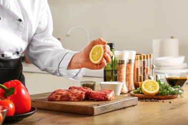 Erkek aşçı mutfaktaki çiğ ete limon sıkıyor.