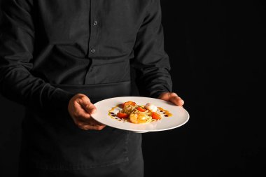 Siyah arka planda lezzetli makarnalı erkek aşçı, yakın plan.