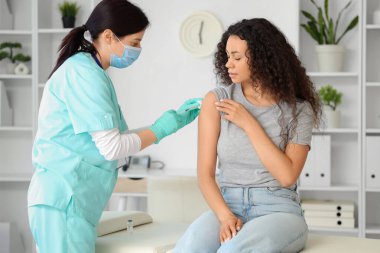 Kadın doktor klinikte Afro-Amerikan kadın aşılıyor.