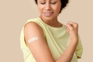 Tıbbi bandı olan genç Afro-Amerikalı kadın bej arka plandaki aşıdan sonra kaslarını gösteriyor, yakın plan.