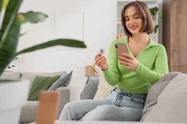 Evde cep telefonu kullanan bitcoin 'li genç bir kadın.