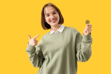 Sarı arka planda Bitcoin 'i işaret eden genç bir kadın