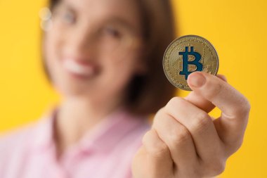 Sarı arka planda bitcoin 'i olan genç bir kadın, yakın plan.