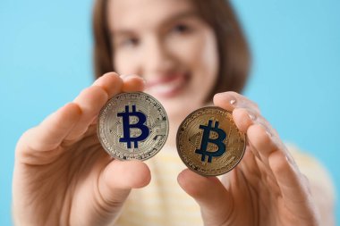 Mavi arka planda bitcoin 'leri olan genç bir kadın, yakın plan.