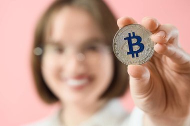 Pembe arka planda bitcoin 'i olan genç bir kadın, yakın plan.