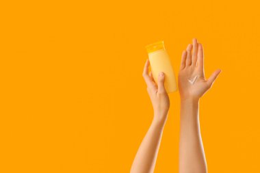 Sarı arka planda, elinde güneş kremi lekesi olan bir kadın.