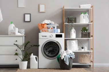 Çamaşır makinesi, kirli çamaşırlar ve raf ünitesi olan hafif çamaşır odasının içi.