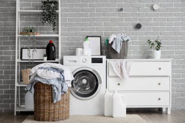 Çamaşır makinesi, çamaşır sepeti ve şifoniyeri olan şık bir banyo.