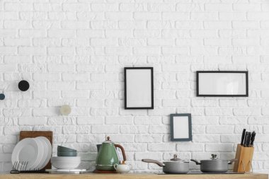 Mutfaktaki beyaz tuğla duvarda çatal bıçak ve boş çerçevelerle sayaç.