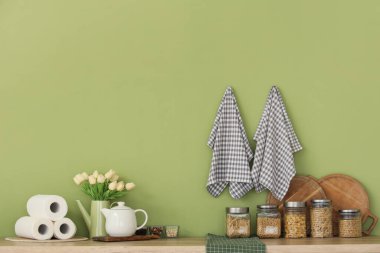 Çaydanlıklı makarna kavanozları, laleler ve kağıt havlular mutfaktaki yeşil duvarın yanındaki tezgahlarda.