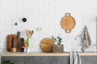 Mutfaktaki beyaz tuğla duvarın yanında lavabo ve çatal bıçaklarla tezgah.