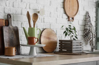 Mutfaktaki beyaz tuğla duvarın yanındaki tezgahta farklı aletler var.