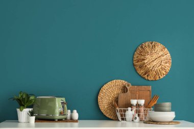 Mavi duvarın yanında ekmek kızartma makineli mutfak aletleri ve bitkiler var.