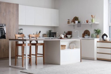 Masası, tezgahı ve çatalı olan aydınlık mutfağın içi.