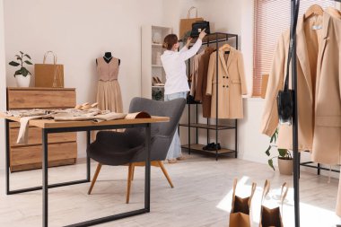 Kadın giyim stilisti. Stüdyodaki raftan çanta alıyor.