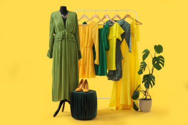 Sarı arka planda manken, puf ve bitki içeren elbise askısı.
