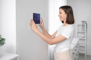 Genç, mutlu bir kadın odasındaki duvarda akıllı ev güvenlik kontrol paneli kullanıyor.